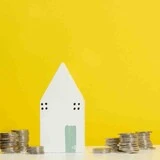 Informácie o dotáciách na rekonštrukciu domov Miniatúra bieleho domu na žltom pozadí s mincami