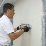 Muž aplikujúci fasádnu omietku na dom.