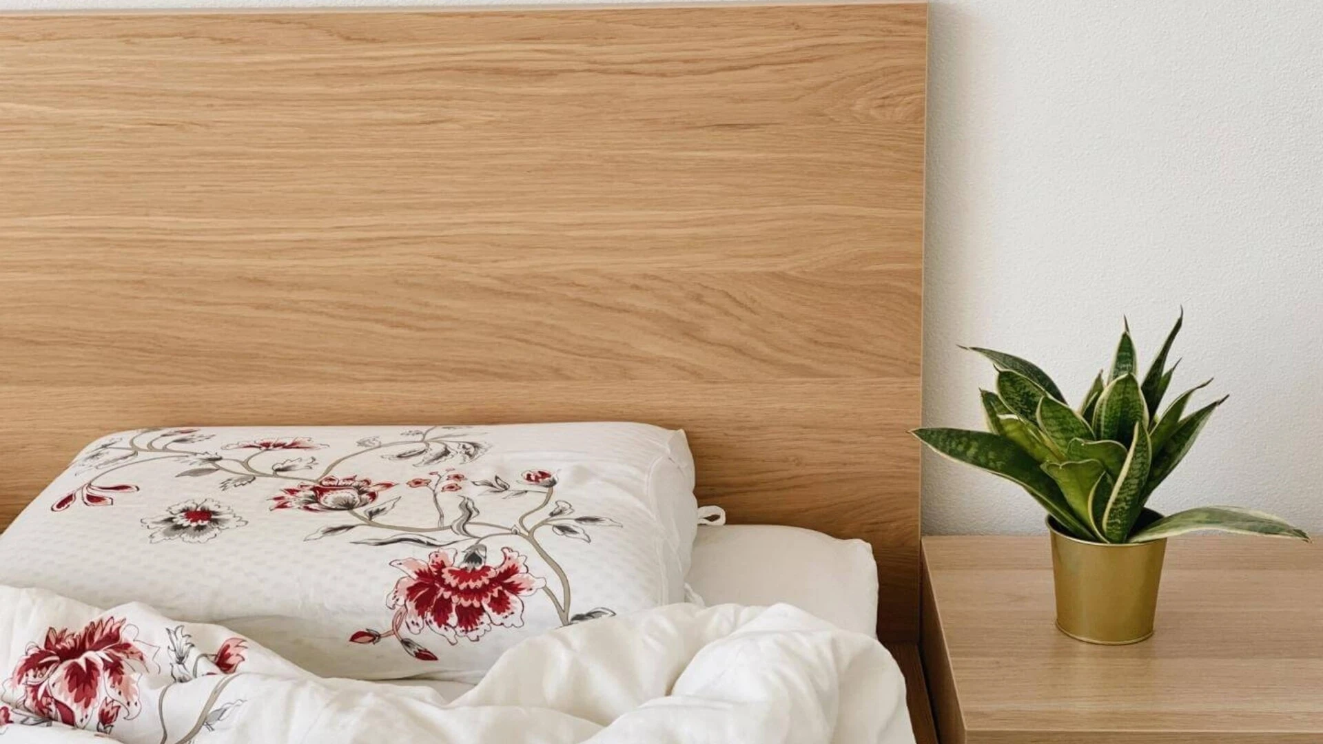 Neustlaná posteľ a rastlina na nočnom stolíku