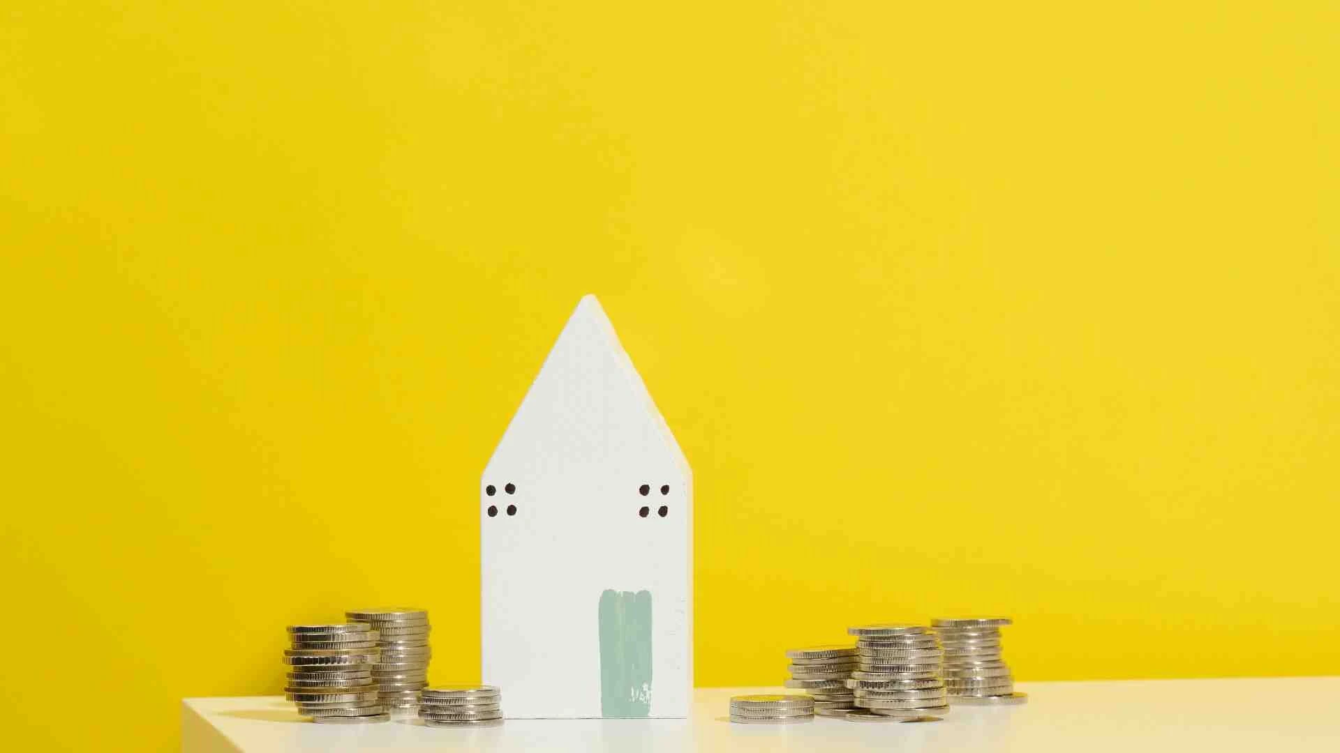 Miniatúra bieleho domu na žltom pozadí s mincami