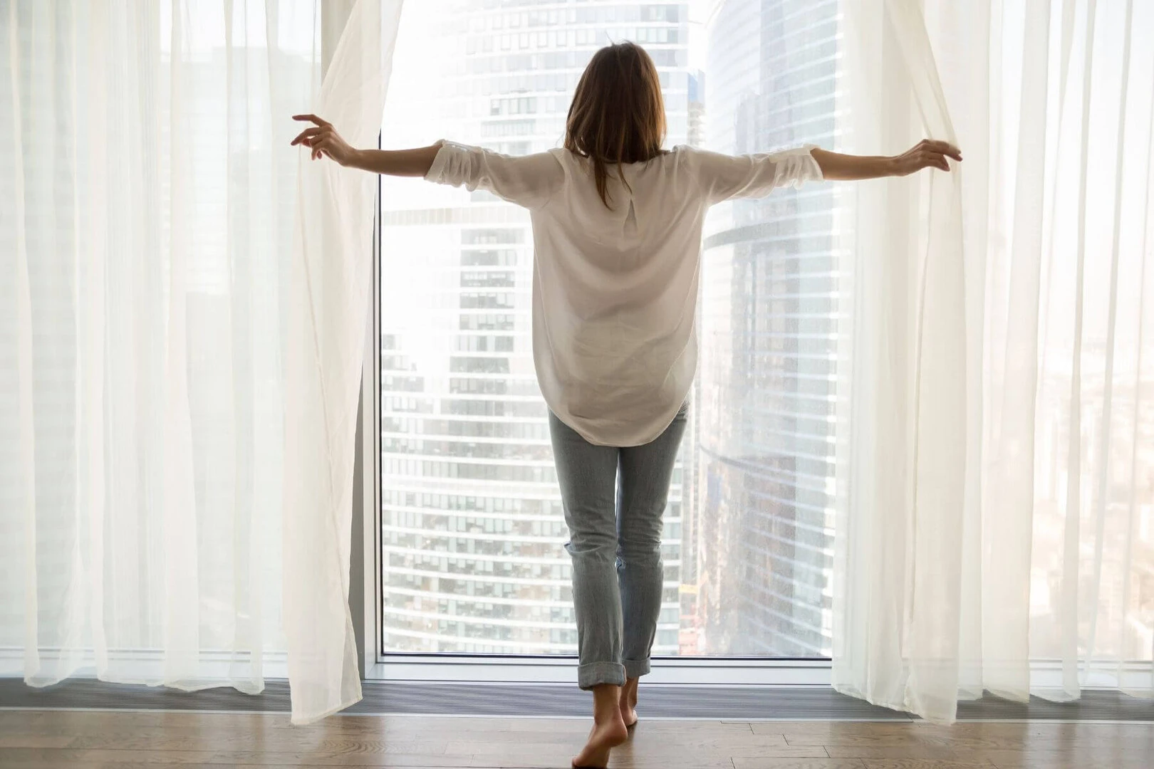 Žena odostiera závesy na veľkom okne v byte