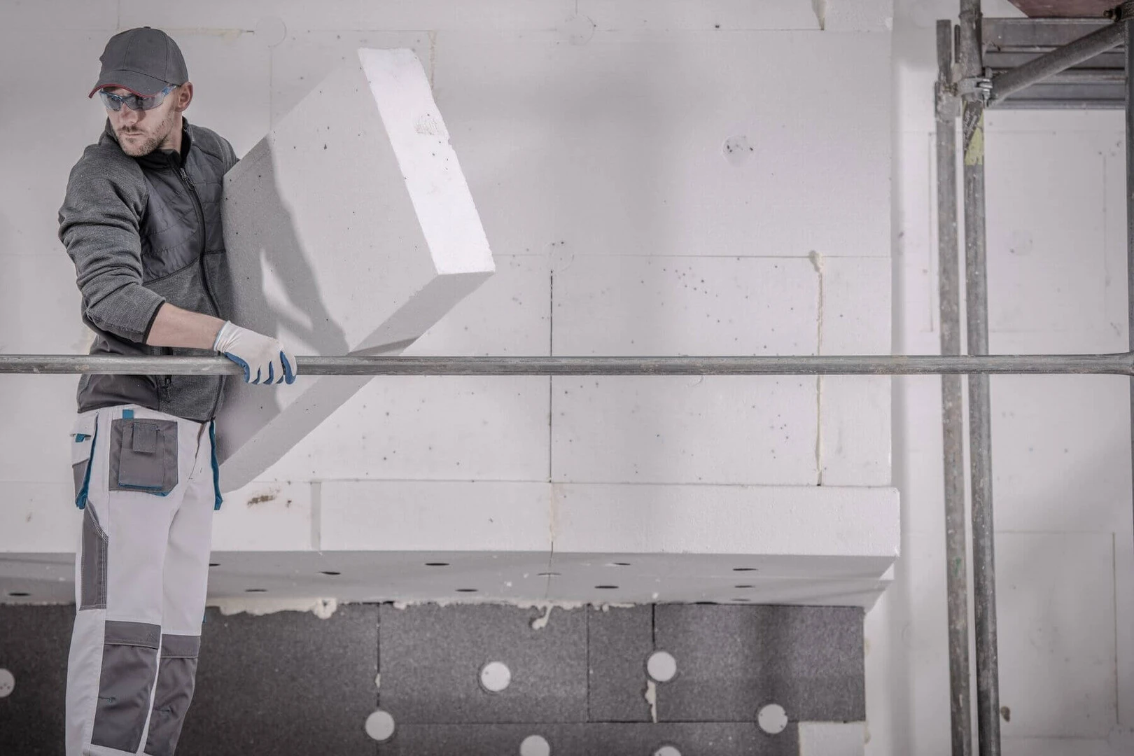 Robotník drží biely polystyrén na zateplenie na lešení