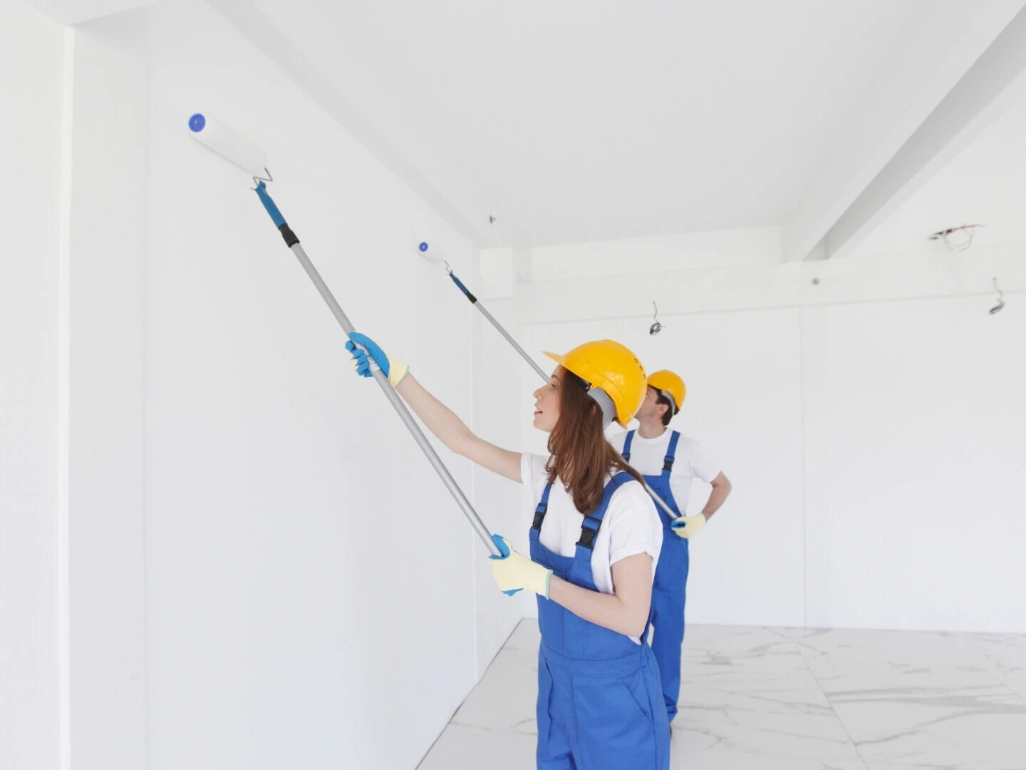 Žena a muž malujúci stenu valčekom na teleskopickej tyči
