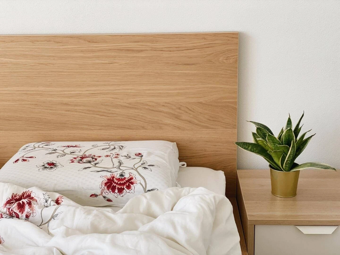 Neustlaná posteľ a rastlina na nočnom stolíku