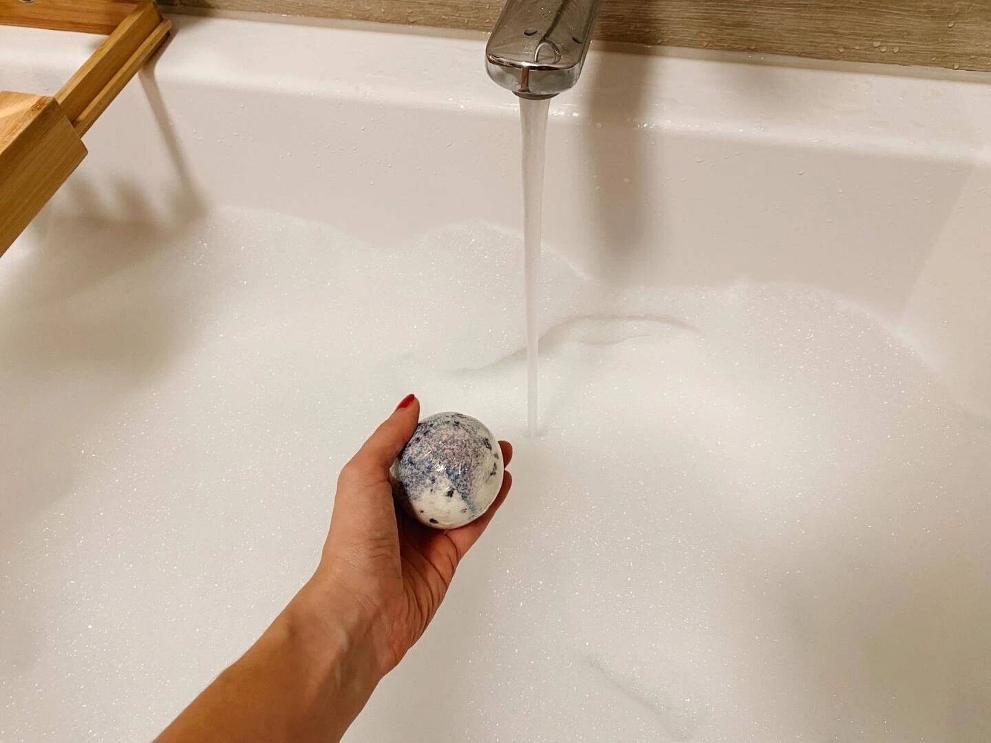 Šumivá bomba do kúpeľa v ruke nad napustenou vaňou