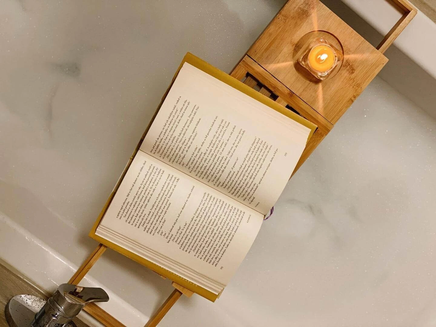 Otvorená kniha a sviečka položená na tácke nad kúpeľom s penou