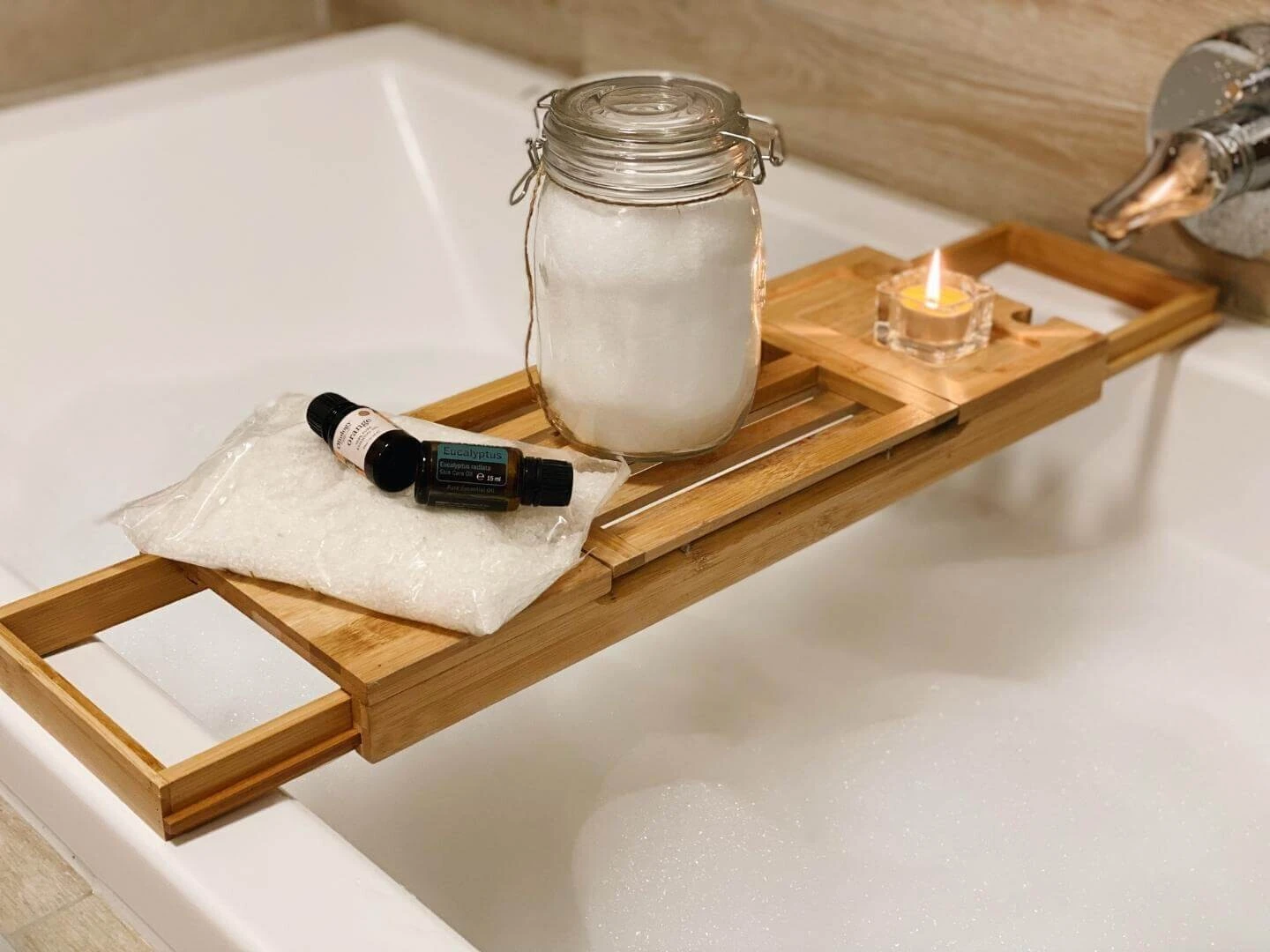 Soľ do kúpeľa a esenciálne oleje na tácke položenej na napustenej vani.
