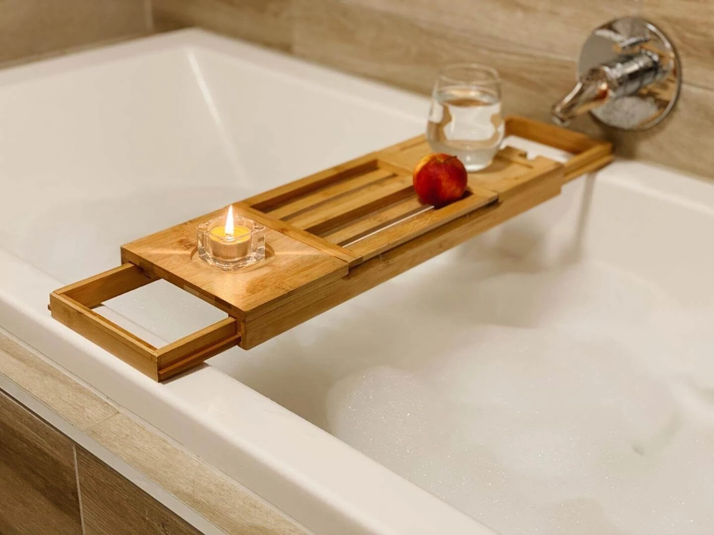 Pohár vody, jablko a sviečka položená na stolčeku na napustenej vani s penou.