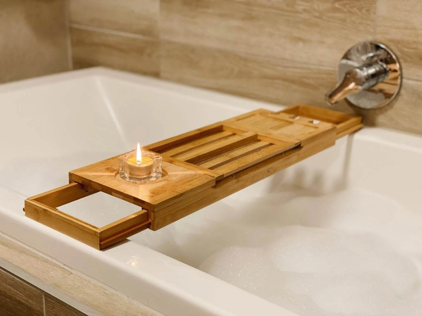 Zapálená medová sviečka na bambusovom stolčeku položenom na vani.