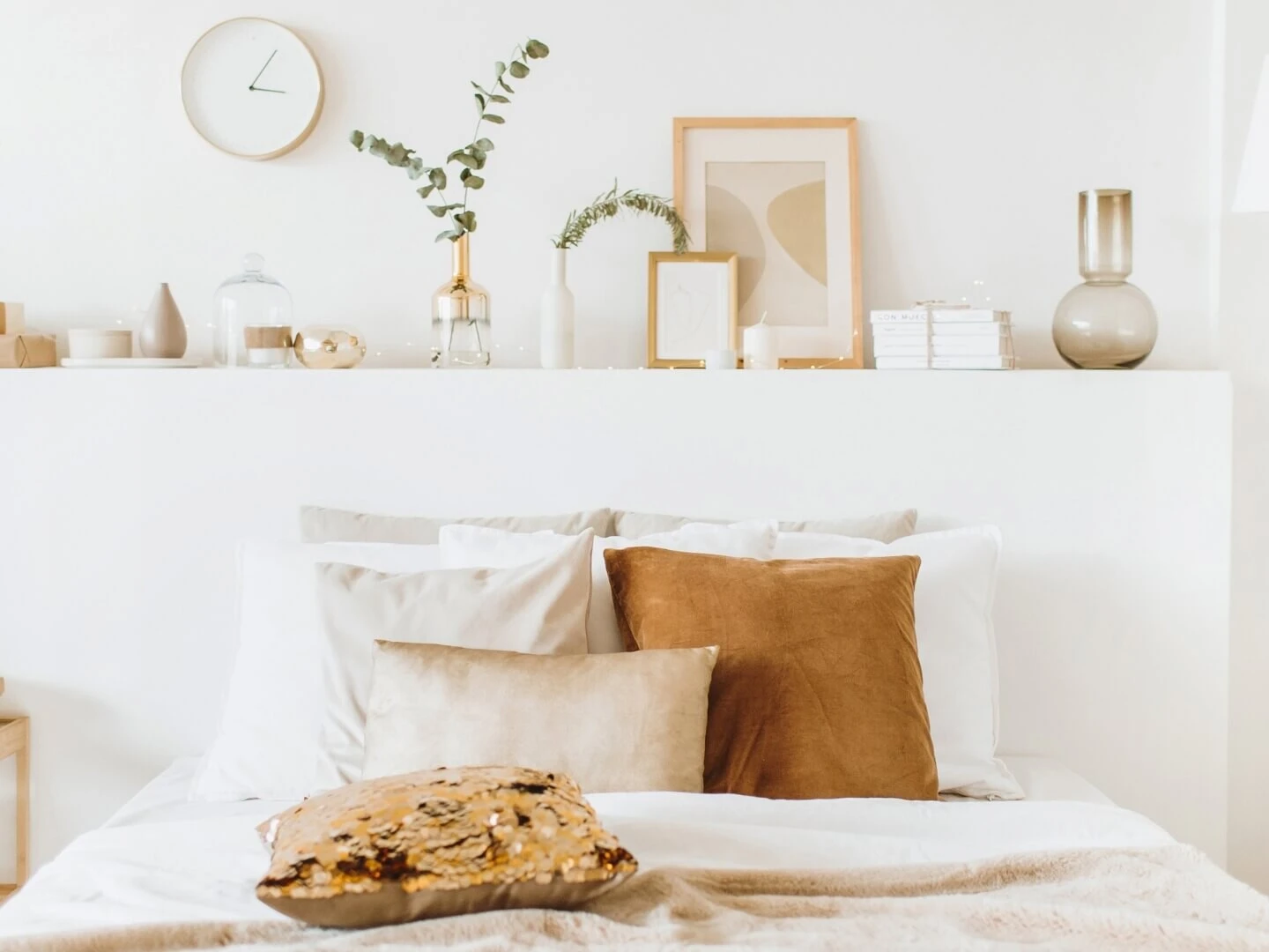 Spálňa s poličkou nad posteľou a rôznymi dizajnovými dekoráciami v prírodných farbách.