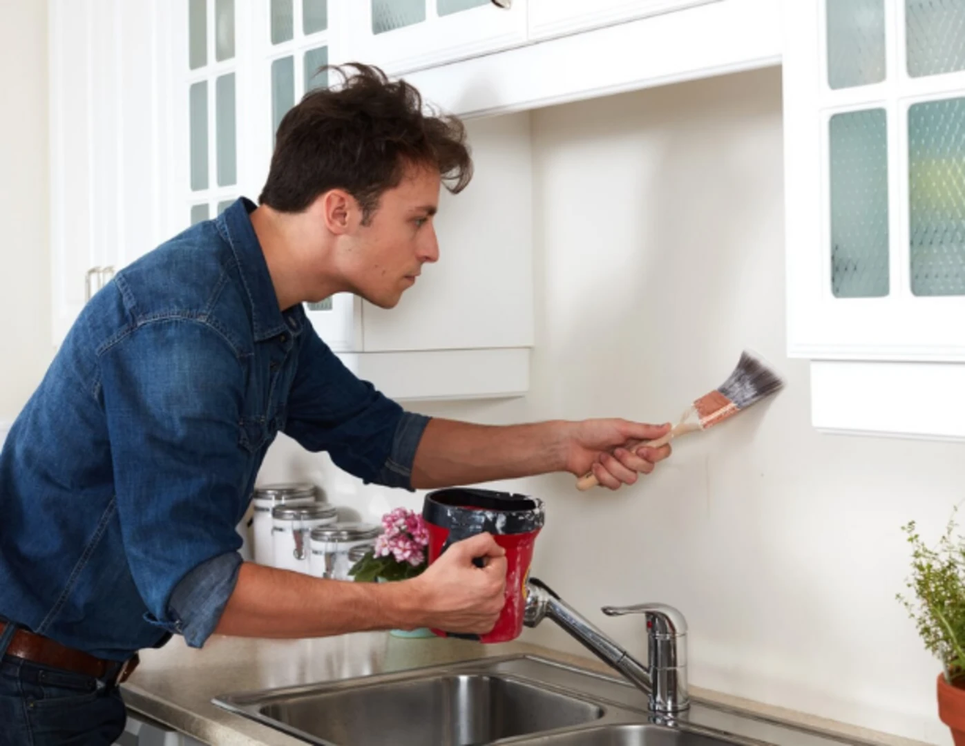 Muž maľujúci steny kuchyne bielou farbou.