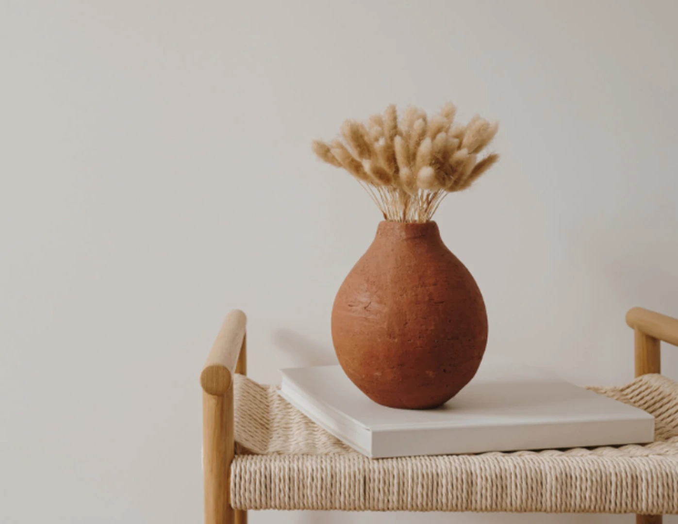 Terakotová váza so sušenou trávou na prútenom konferenčnom stolíku.