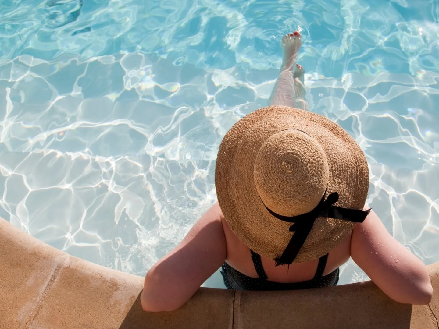 Žena s klobúkom oddychujúca v bazéne na dovolenke.