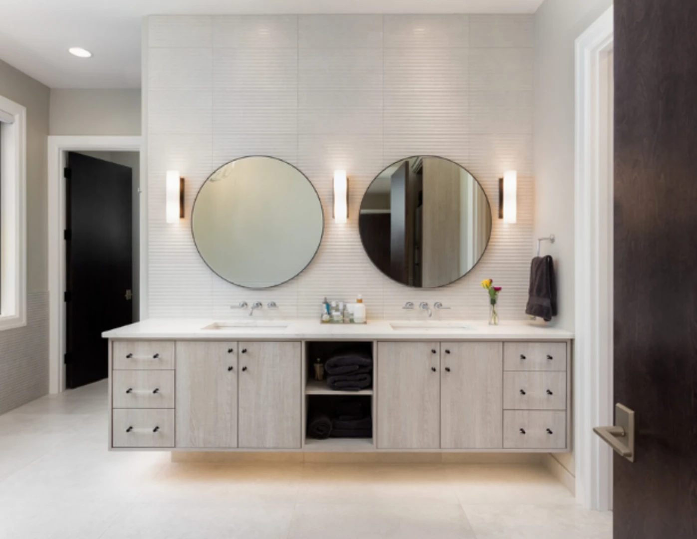 Nástenné osvetlenie v kúpeľni vedľa okrúhlych zrkadiel.