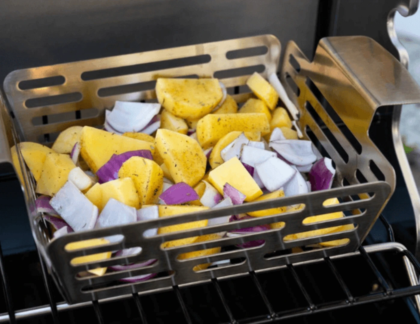 Zemiaky a červená cibuľa v nerezovom grilovacom košíku.