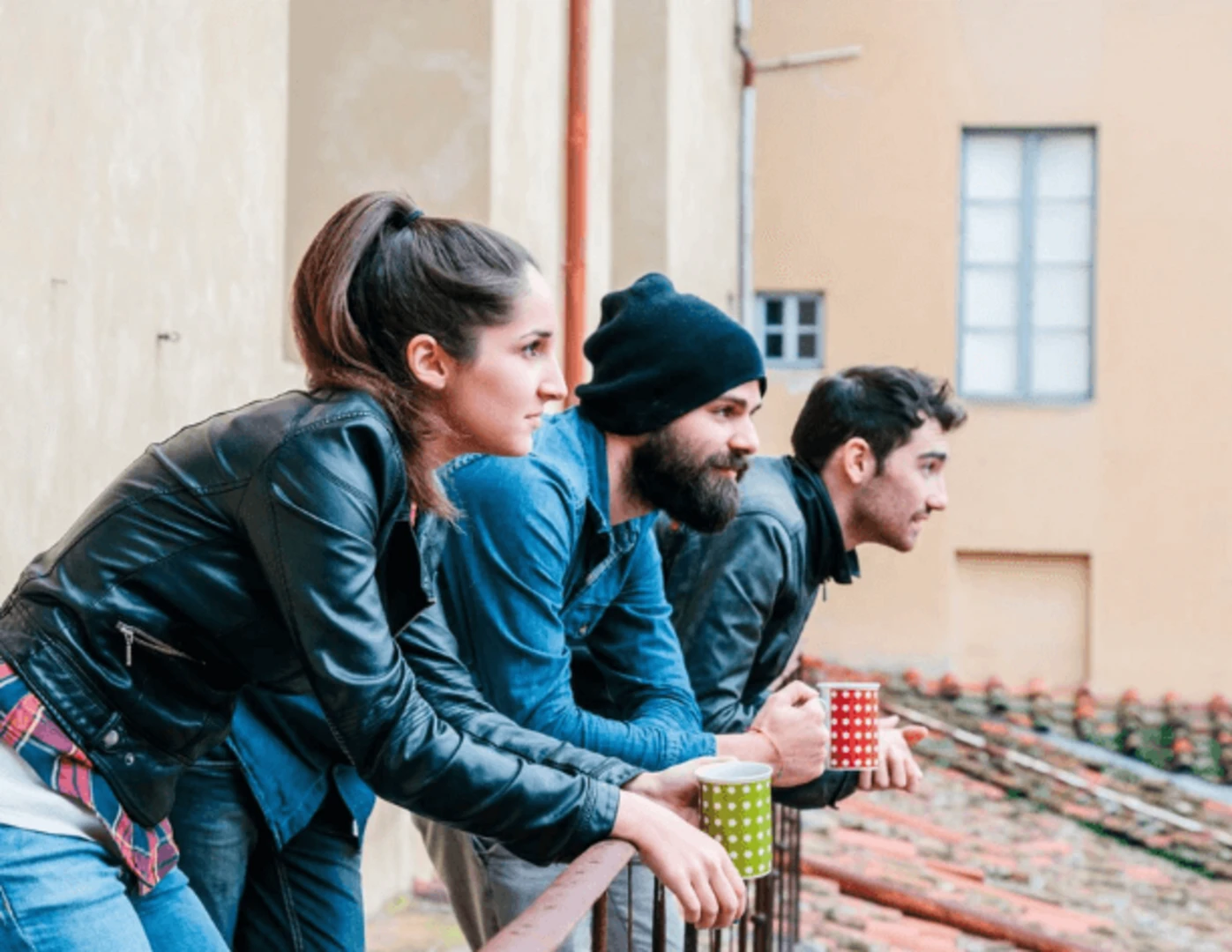 Osoby opierajúce sa o balkónové zábradlie s kávou v rukách.