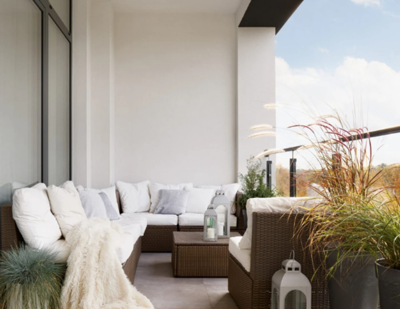 Útulný balkón s množstvom vankúšov na ratanovom sedení.