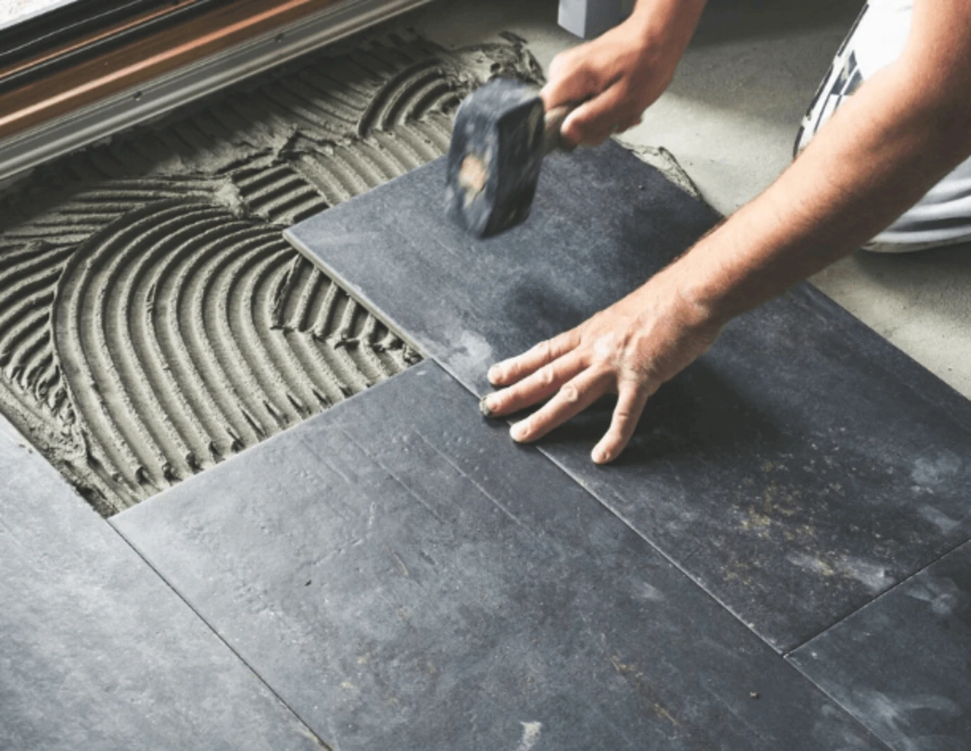 Pracovník umiestňuje keramické dlaždice na lepivý podklad.