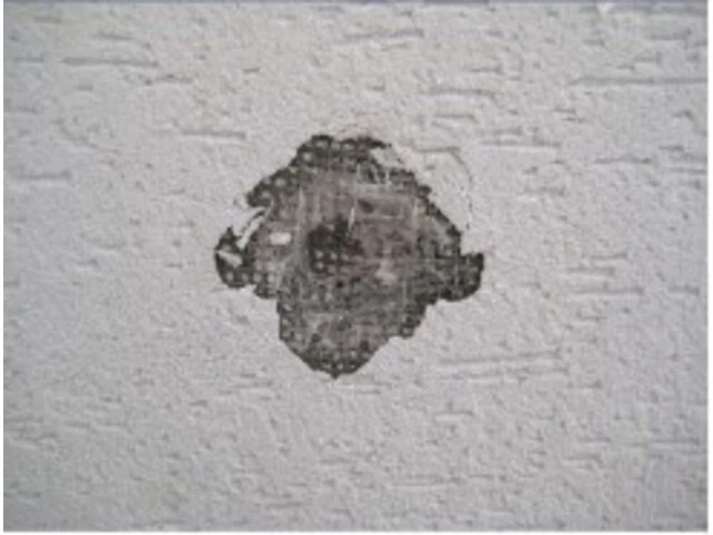 Diera na bielej stene domu, poškodená fasáda