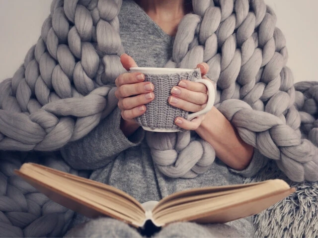 Žena číta knihu zabalená v teplej deke so šálkou čaju