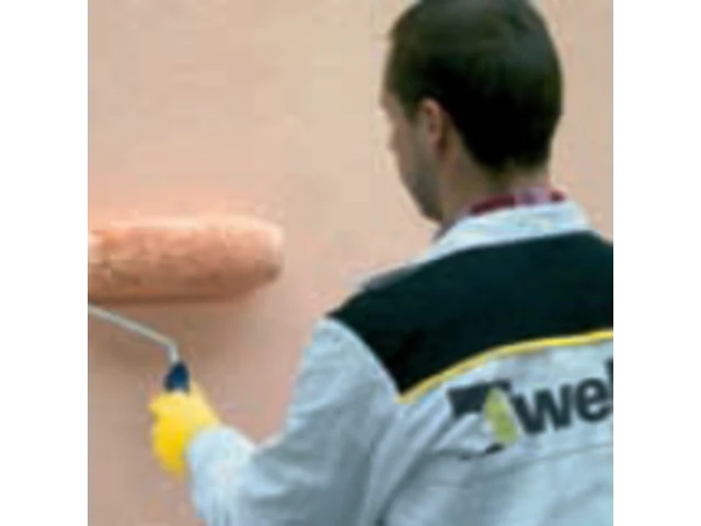 ružová stena sa natiera valčekom. Muž má weber mikinu a čierne vlasy