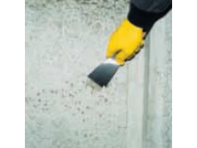 Ruka ktorá pripravuje podklad škrabkou. Má žltú rukavicu