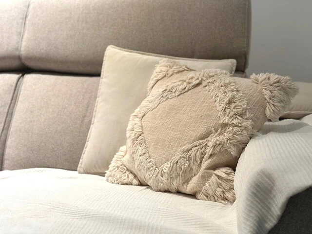 Sivá sedačka s bielou dekou a bledými dekoračnými vankúšmi.