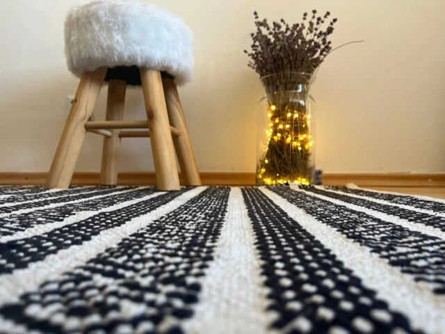 Čierno-biely koberec s bielou kožušinovou taburetkou a vázou so svetielkami.