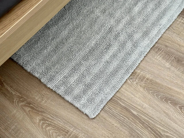 Malý obdĺžnikový šedý koberček pri posteli.