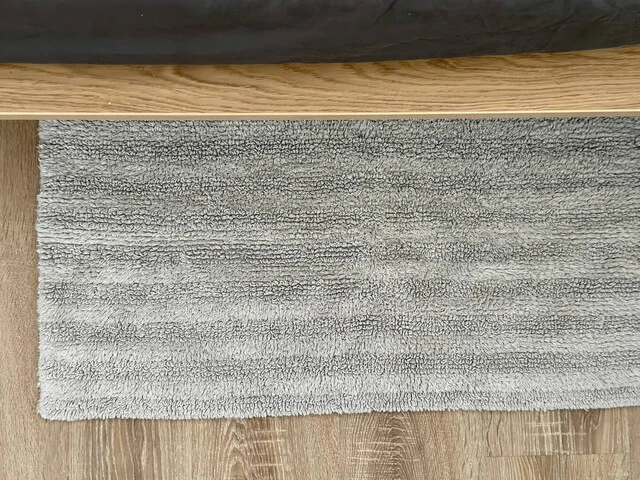 Malý šedý koberec pri posteli.