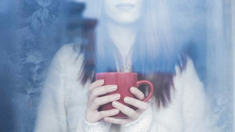 Aby vás zima nezaskočila žena s červenou šálkou v zime za sklom