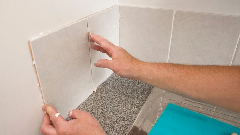 ruky ktoré lepia obklad na stenu