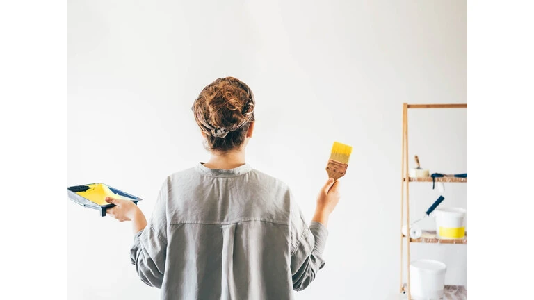 Žena pripravujúca sa na maľovanie steny žltou farbou